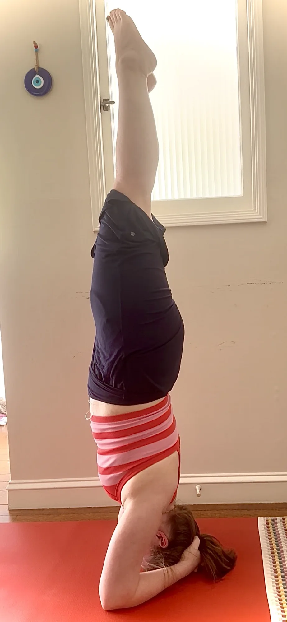 Sara practicing a headstand on a red yoga mat