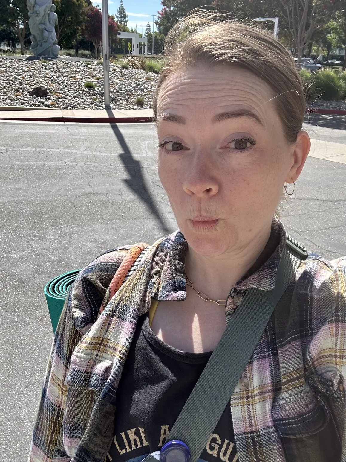 Sara taking a sunny outdoor selfie with a rolled yoga mat